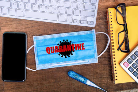 Quarantine and work online from home duringt Covid-19 pandemic with protecive mask, smart phone and computer on deskの写真素材