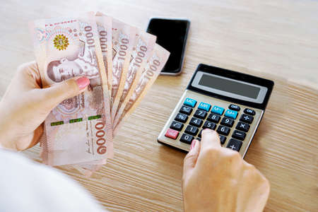woman hand holding thai paper currency and counting saving money on calculatorの写真素材