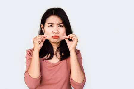 unhappy Asian woman hand pulling her fat skin on cheeks ,aging and overweight conceptの写真素材