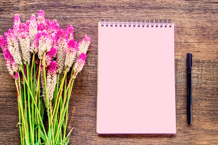 beautiful pink flower ,blank paper notepad and pen on wooden table