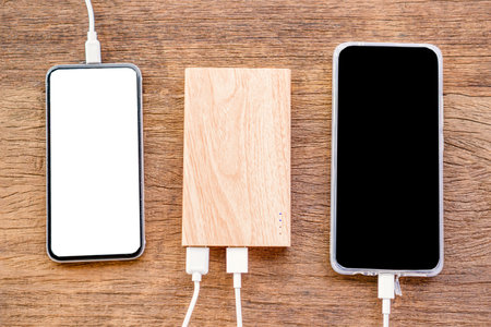 tech device charge sharing concept with smart phone charging with power bank on wooden table