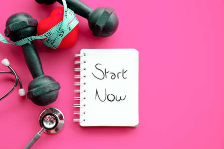start now for sport diet and heart healthy concept with dumbbells ,measuring tape, stethoscope and note pad on pink backgroundの写真素材