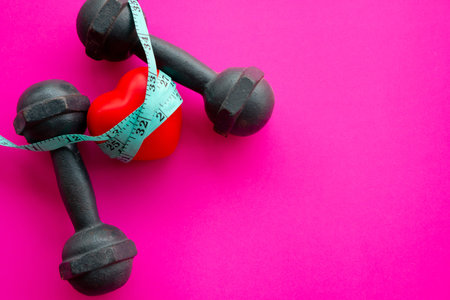 heart healthy and sport diet concept with dumbbells, measuring tape on pink backgroundの写真素材