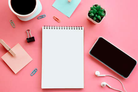 business flat lay on pink background with open note pad ,smart phone, paper note and coffee cupの写真素材