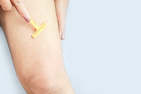 woman hand shaving hairy leg by razor blade closeup
