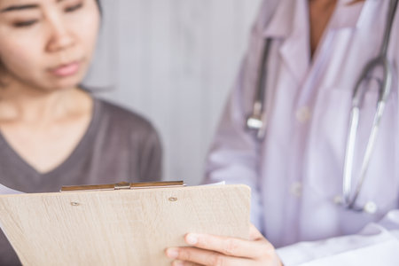 doctor talking to female patient and showing blood test on clipboard at a hospitalの写真素材