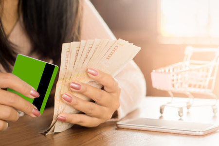 business woman hand holding Thai baht banknotes money with credit card for shopping online