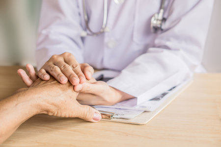 doctor holding hand and comforting old patient in a hospital during their appointmentの写真素材