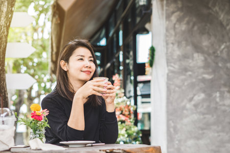 young beautiful Asian woman drinking coffee outdoors sitting at coffee shopの写真素材