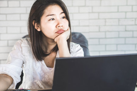 unmotivated Asian female worker sitting at desk bored to work thinking of 
quitting jobの写真素材