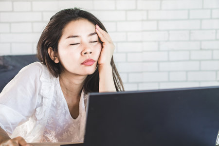 tired Asian woman sleepy taking a nap at work sitting at office deskの写真素材