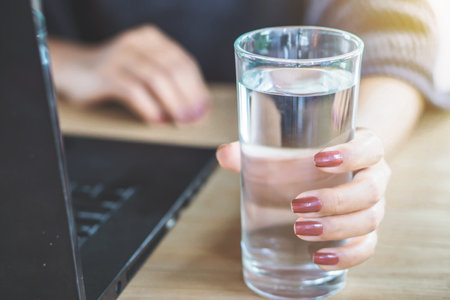business woman drinking fresh water while working on computer laptop at office desの写真素材