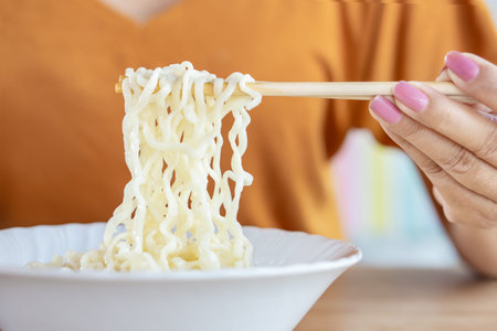 closeup woman hand holding chopsticks eating hot noodle in cup