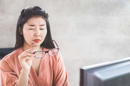 Asian woman worker suffering from eye strain taking off her eyeglasses tired from working on computer screenの写真素材