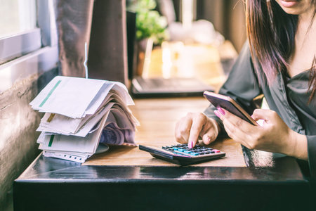 woman hand calculating her monthly expenses and debt during tax season with financial bills on deskの写真素材