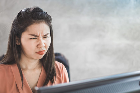 unhappy Asian worker bored with working on computer at workplaceの写真素材