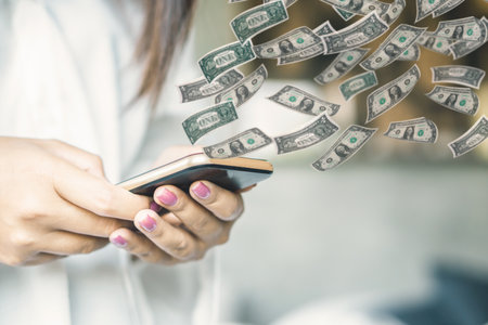 woman hand holding smart phone transfer money online with paper currency flyingの写真素材