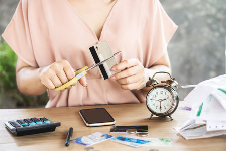 debt free concept with woman hand cutting credit card by scissors with alarm clock on deskの写真素材