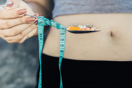 overweight woman hand holding spoon with diet pills , unhealthy lifestyle conceptの写真素材