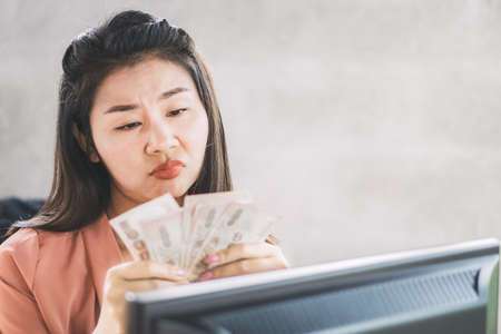 sad Asian female worker hand holding paper currency unhappy with less salaryの写真素材