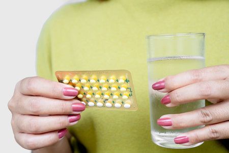 woman hand taking birth control or contraceptive pills with glass of water