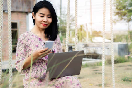 business Asian woman working outdoors hand using smart phone and laptop connected to internet, work from anywhere conceptの写真素材