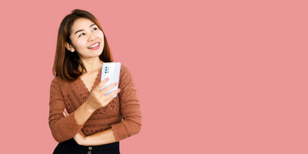 happy Asian woman holding smart phone standing looking up over pink banner background