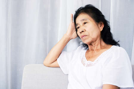 stressed old Asian woman sitting lonely at home feeling sad and depressedの写真素材