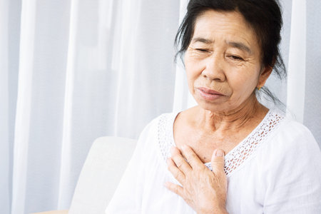 old Asian woman having problem with shortness of breath, difficult breathing hand touching her chestの写真素材