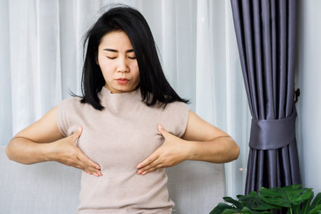 Asian woman checking her breast cancer self examination sitting on sofa