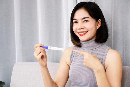 happy Asian woman smiling hand holding at pregnancy test showing positive result
