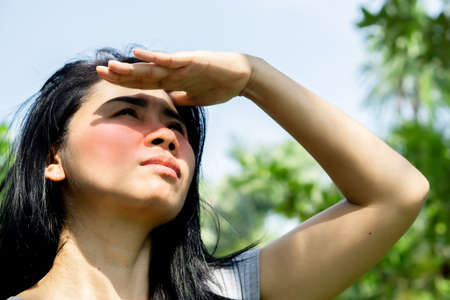 Asian woman having problem sunburn redness on face skin hand cover her face to protect ultraviolet from sunlight standing outdoors under sunnyの写真素材