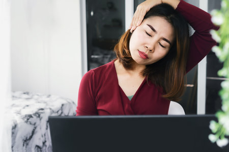 Asian business woman stretching her tired and painful neck to relax muscle sitting too long on computerの写真素材