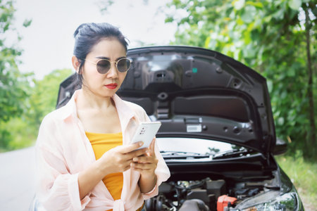 upset Asian woman using smart phone calling for help with broken car stopped on roadsideの写真素材