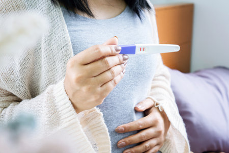 closeup woman hand showing positive result of pregnancy test another hand holding her stomachの写真素材