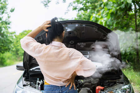 Asian woman having problem with broken, overheat car while driving alone on the road standing with smoke from the engineの写真素材
