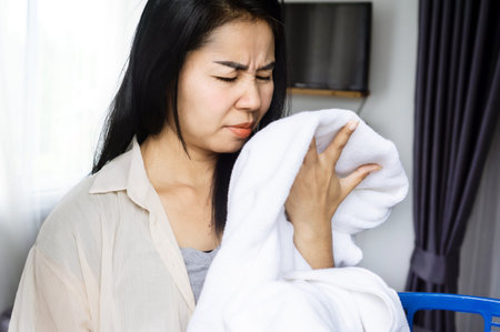 Asian housewife smelling stinky towel, woman having problem with bad smell from clothesの写真素材