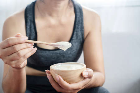 a healthy woman in sportswear eating yogurt after doing sport hand holding bowl and spoon closeupの写真素材