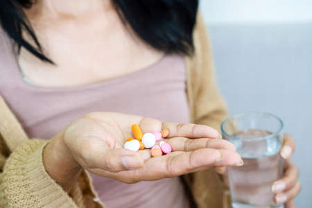 closeup handful of medicines, hand woman hand taking overdose pills with glass of waterの写真素材