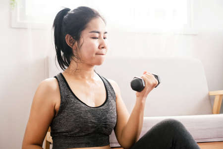 sport Asian woman weight lifting dumbbells exercise and workout at homeの写真素材