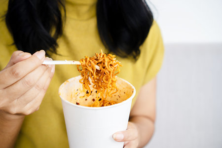 woman hand holding cup of spicy noodles, a woman eating noodle closeupの写真素材