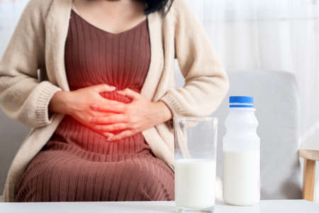 woman holding stomachache after drinking a glass of cow milk feeling bad, discomfort because of expired date, indigestion conceptの写真素材