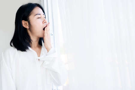 sleepless Asian woman yawning after waking up in the morning feeling tired and sleepyの写真素材