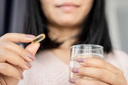 healthy eating concept with Asian woman taking fish oil hand holding capsule vitamin and a glass of waterの写真素材
