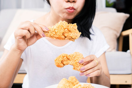 Asian woman over eating oily, junk food hand holding fried chicken closeupの写真素材