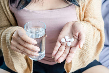 closeup woman hand taking overdose pill hand holding glass of waterの写真素材