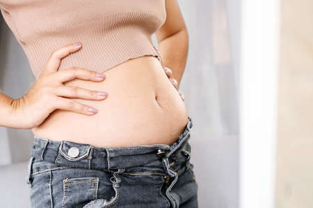 closeup belly fat woman checking her body in front of a mirror wearing jeansの写真素材