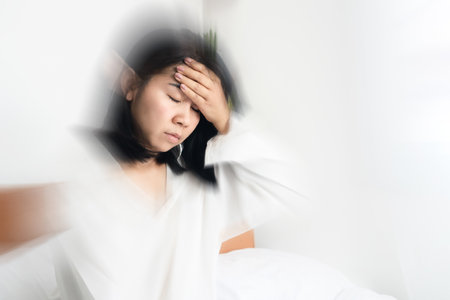 Asian woman fainting ,dizziness after wakeup in bed hand holding her headacheの写真素材