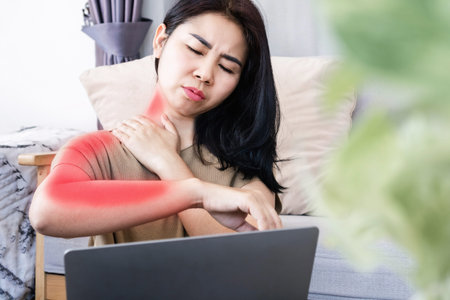 Asian woman suffering from neck pain spreading to shoulder and down arm caused by overworked on a computer with bad postureの写真素材