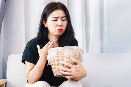 unwell Asian woman vomiting caused by stomach flu, Food allergies hand holding binの写真素材
